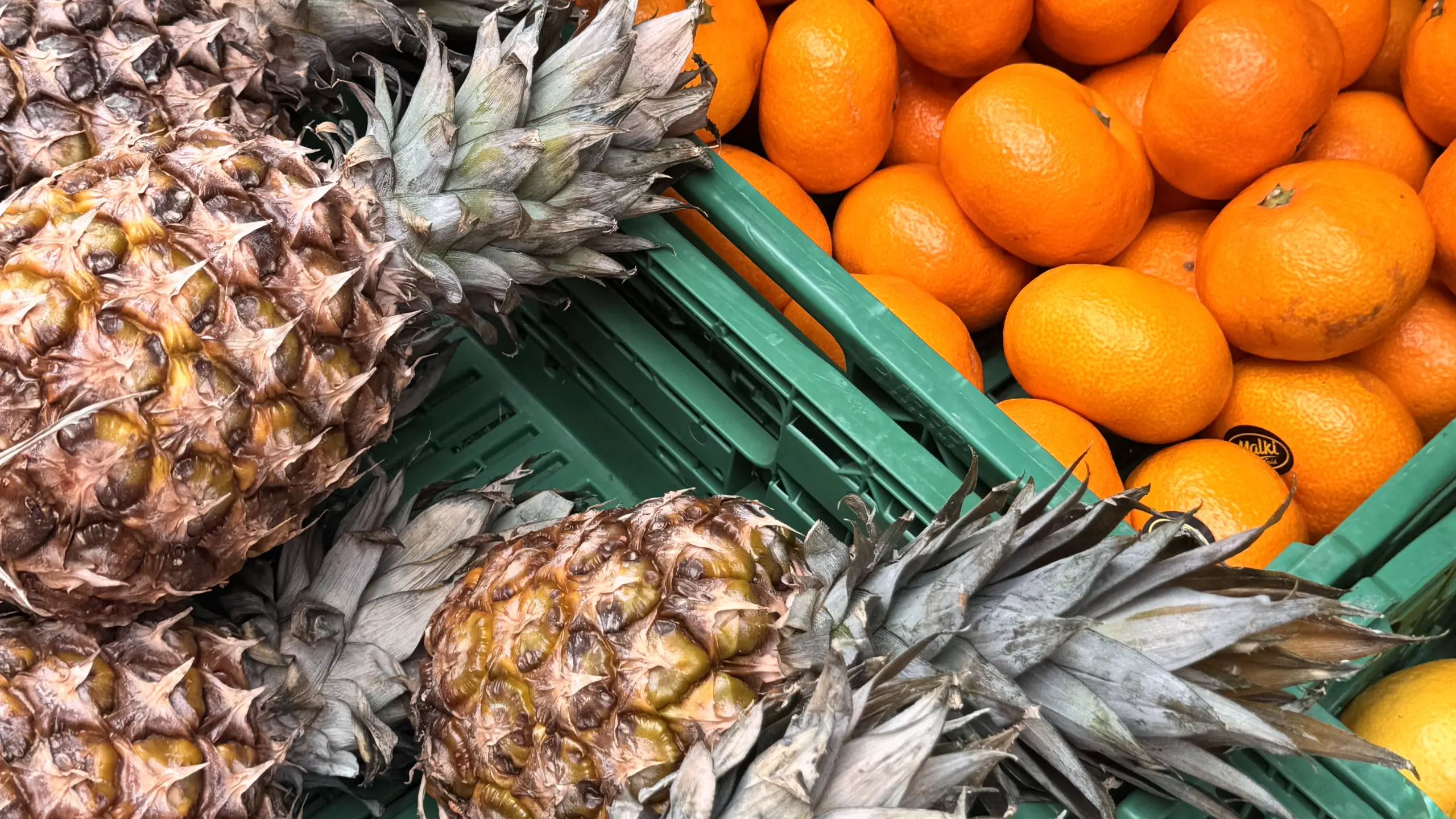 Fresh pineapples and oranges in crates on a market produce stall